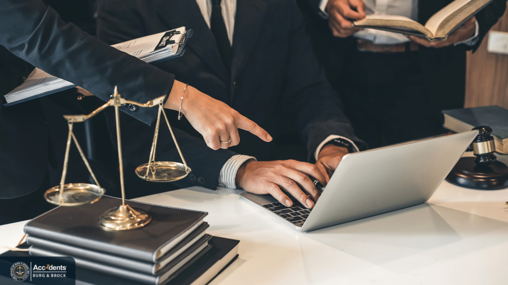 Legal team reviewing a case on a laptop beside brass scales of justice and law books
