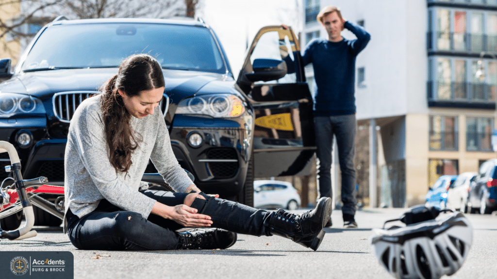 Injured cyclist sitting on the road after a collision while a driver stands beside an SUV