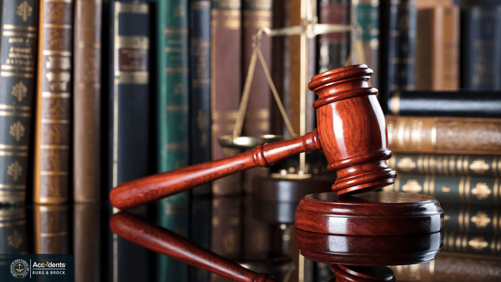 Gavel resting on a desk in front of a shelf of law books and a set of scales
