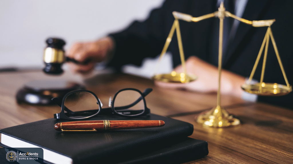 Gavel, reading glasses and a pen on a notebook beside a set of brass scales on a desk