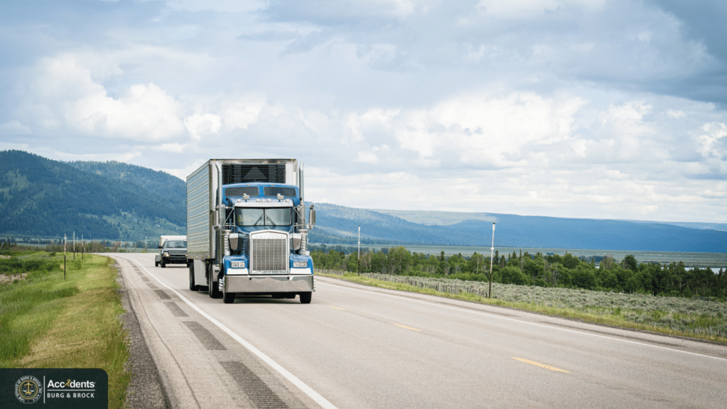 Blue semi truck pulling a trailer along a two-lane highway with mountains in the background